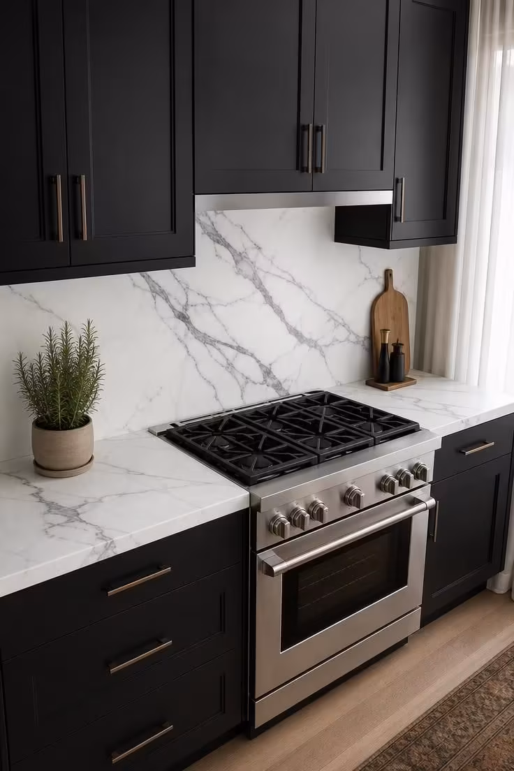 Honed white Calacatta marble slab backsplash with diagonal veining running between matte black upper and lower cabinets in soft diffused natural light.