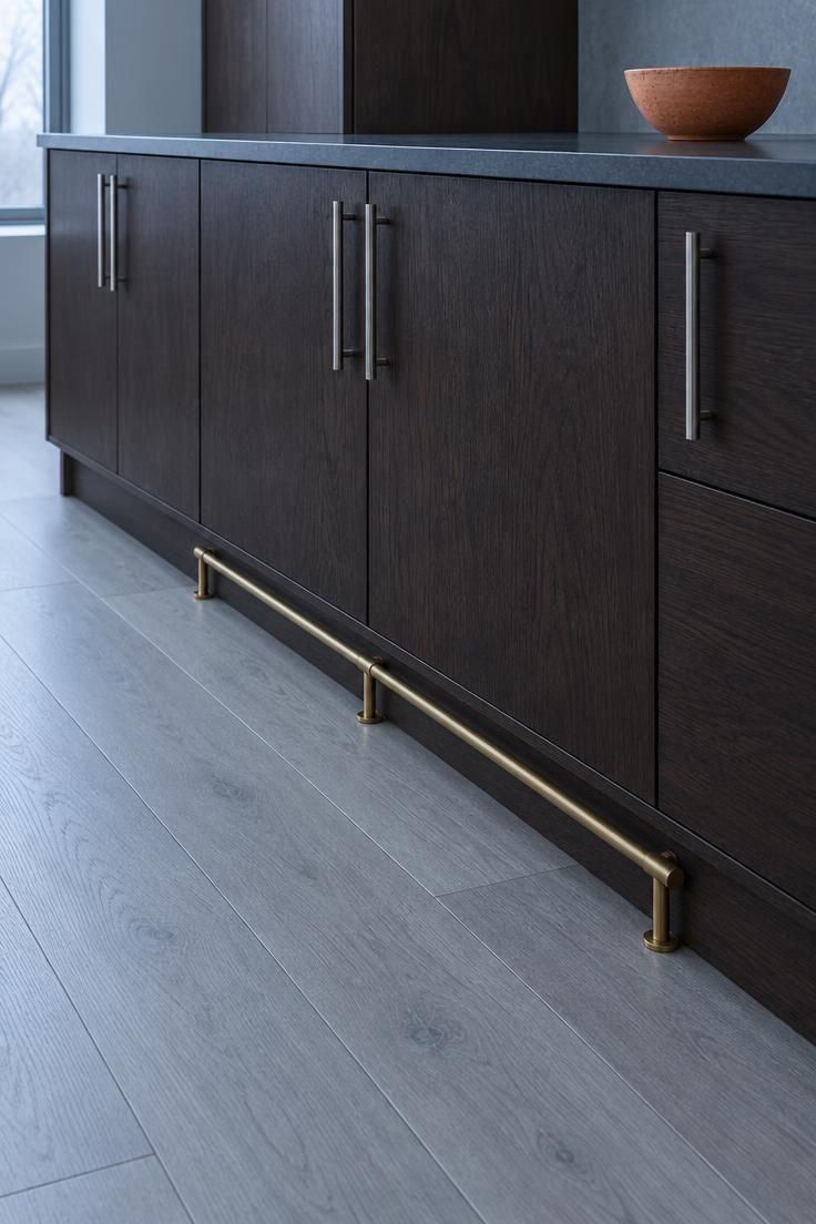 A close view of a dark espresso cabinet base meeting a pale gray floor, with one terracotta bowl as the only warm note.