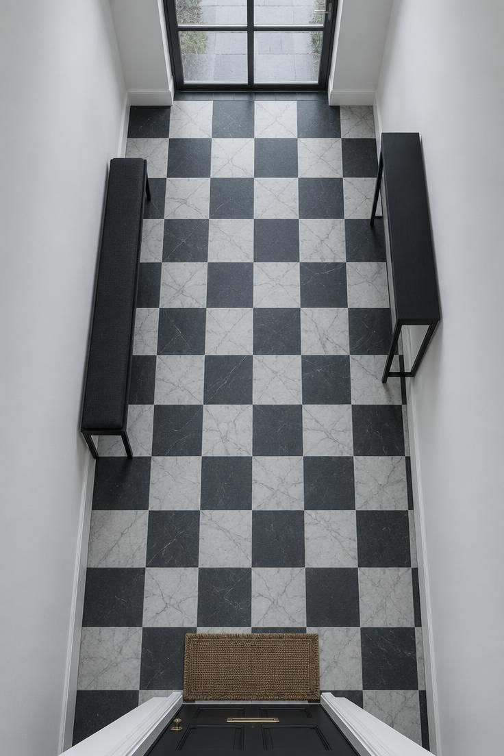 13 Clever Large Hallway Ideas to Make Yours Feel Like a Room 10 An overhead view of a wide hallway floor laid in a marble and slate checkerboard pattern, with plain white walls, a single narrow console, and a woven mat at one end.