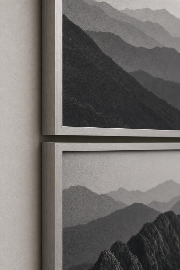 11 Bold Large Wall Decor Ideas That Fill Every Blank Space 4 Close-up detail of two oversized charcoal landscape photographs in matte aluminum frames stacked vertically with a narrow shadow gap between them.