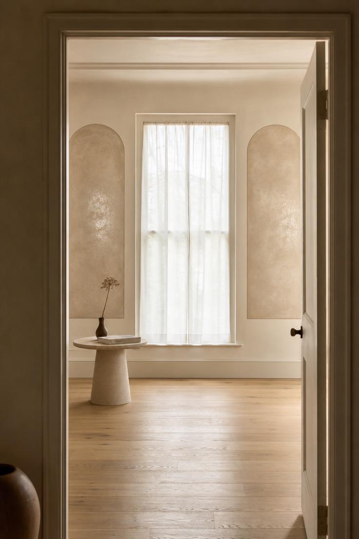 11 Bold Large Wall Decor Ideas That Fill Every Blank Space 8 Two arched Venetian plaster panels in warm putty flanking a tall window viewed from a doorway threshold with soft diffused light.