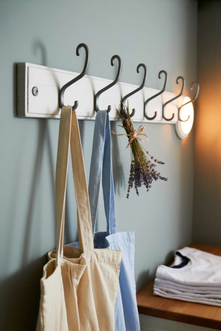 11 Beautiful Laundry Room Wall Decor Ideas That Inspire 10 A row of five matte black iron hooks on a white wood plank against a gray laundry room wall, holding linen bags and dried lavender.