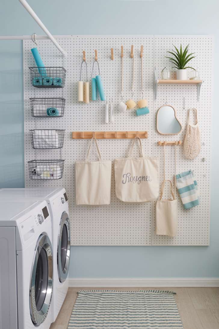 11 Beautiful Laundry Room Wall Decor Ideas That Inspire 8 A white pegboard on a pale blue laundry room wall with wire baskets, wooden pegs holding tote bags, a small mirror, and an air plant on a tiny shelf.
