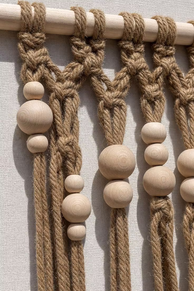 Close-up detail of a natural hemp macrame wall piece with clusters of raw wooden beads in varying sizes under bright midday skylight.
