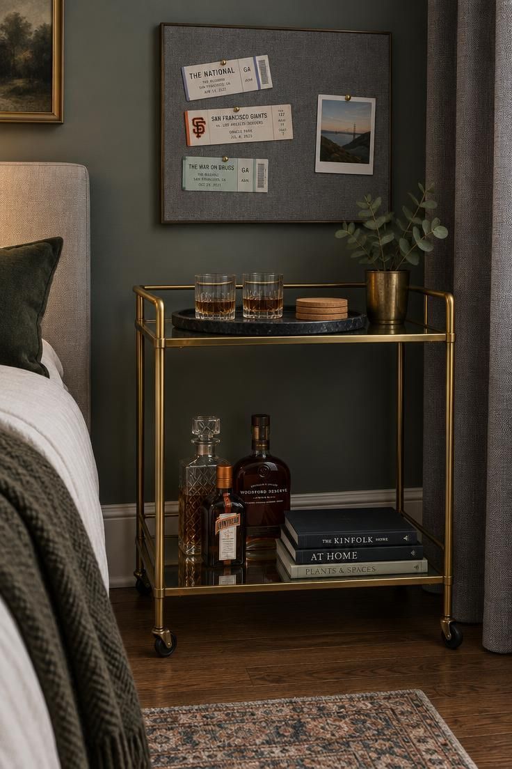 11 Man Cave Bedroom Ideas for a Room That Feels Like Yours 9 Slim brass bar cart with a black tray, two glasses, and cork coasters, positioned in a bedroom corner beneath a gray fabric tackboard holding ticket stubs and a square photo.