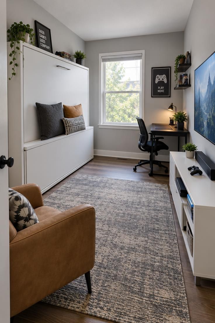 11 Cozy Man Cave Gaming Room Ideas for Solo Nights In 9 Spare bedroom with a closed white fold-down wall bed, black desk and chair, TV on a low white stand, tan armchair, and decorative pillows in bright daylight.