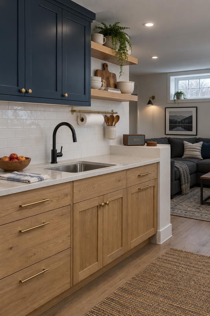 9 Warm Man Cave Kitchen Ideas for Easy Game-Day Hosting 9 A bright kitchen with pale oak base cabinets, ink-blue uppers and floating shelves holding cream stoneware and cutting boards, white subway tile, a stone counter with matte black faucet, and a plaster ledge with a speaker and coasters.