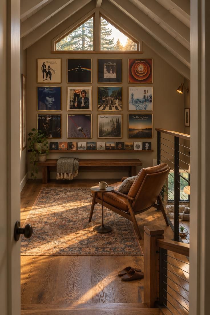 11 Cozy Man Cave Loft Ideas for a Warm Upstairs Escape 1 Stair-top view of a loft with a low walnut bench under the ridge, framed album covers across the gable wall, and a leather chair turned toward a cable railing in warm golden light.