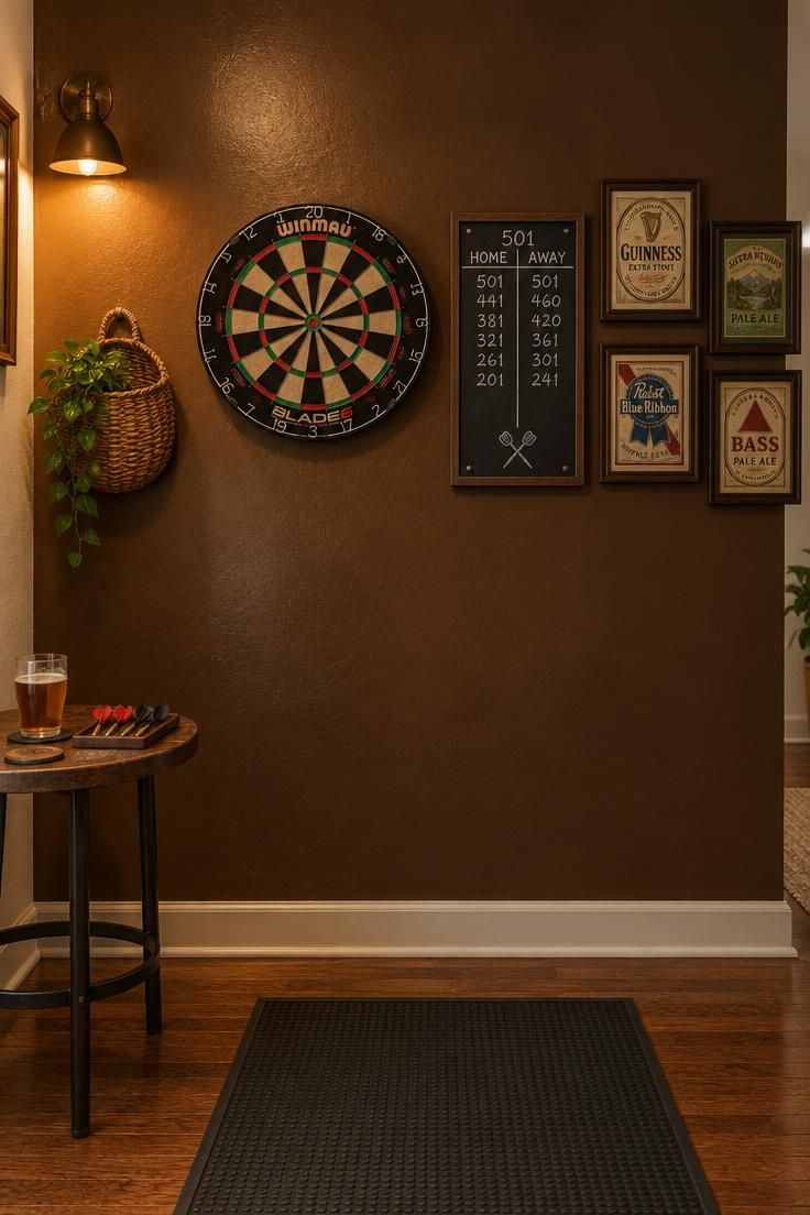 Tobacco brown accent wall with a dartboard, chalk scoreboard, woven wall basket, and framed vintage beer labels against surrounding off-white walls.