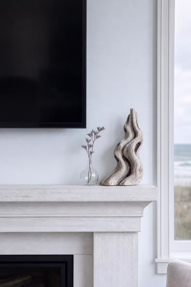 A sculptural piece of weathered driftwood anchoring one end of a whitewashed mantel below a wall-mounted TV