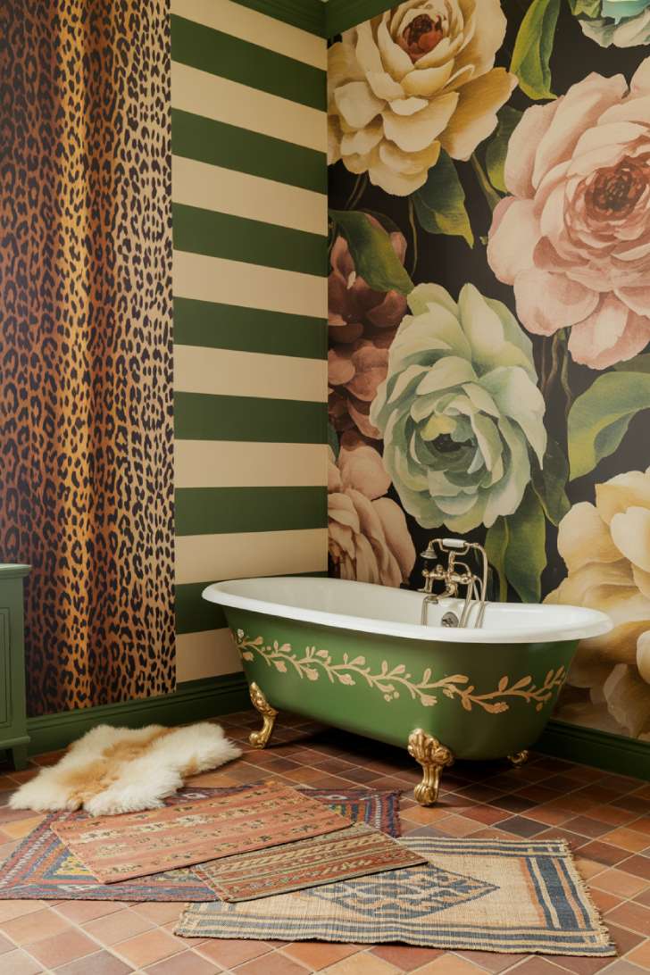 A joyfully eclectic maximalist bathroom with four different wallpapers, a forest green painted roll-top tub, indoor botanical garden, and a dried floral mirror frame