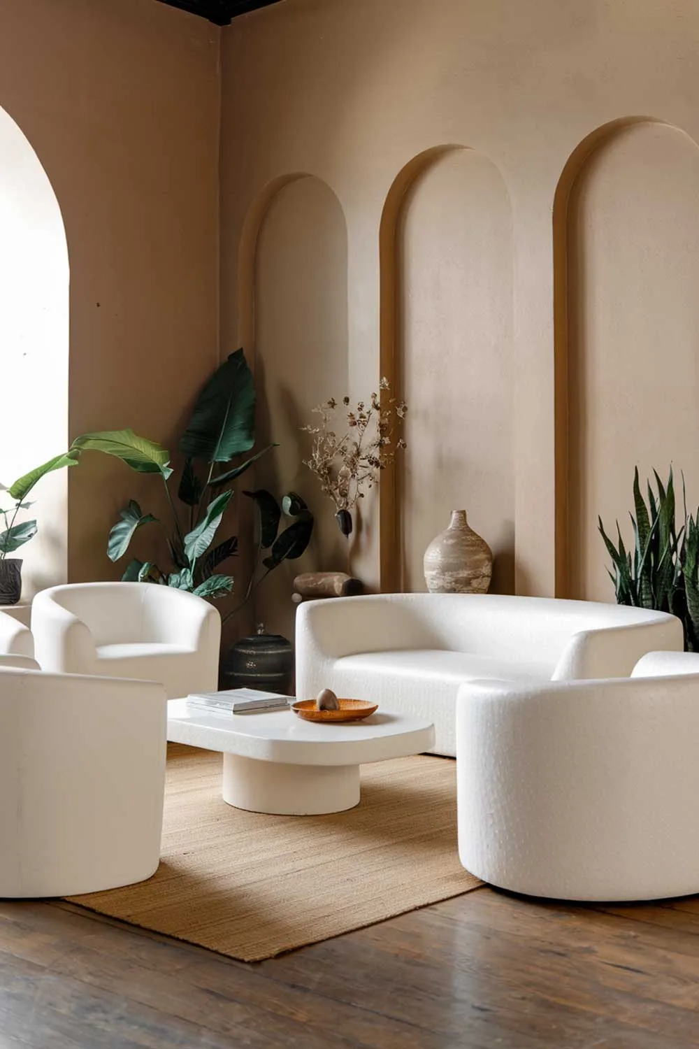 25 Inspiring Minimalist Living Room Ideas with Earth Tones 13 A modern white minimalist living room with earth tones. The room contains a white sofa, a few white chairs, and a white coffee table. There are also some plants in the room. The walls are painted in a beige tone. The floor is made of wood. There are some decorative items, such as a vase and a potted plant.