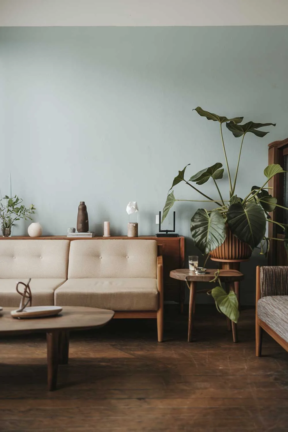 25 Inspiring Minimalist Living Room Ideas with Earth Tones 17 A japandi minimalist living room with earth tones. The room has a beige sofa, a few wooden furniture pieces, and a green plant. The walls are painted in a light blue hue. There is a wooden coffee table and a few decorative items. The floor is made of hardwood.
