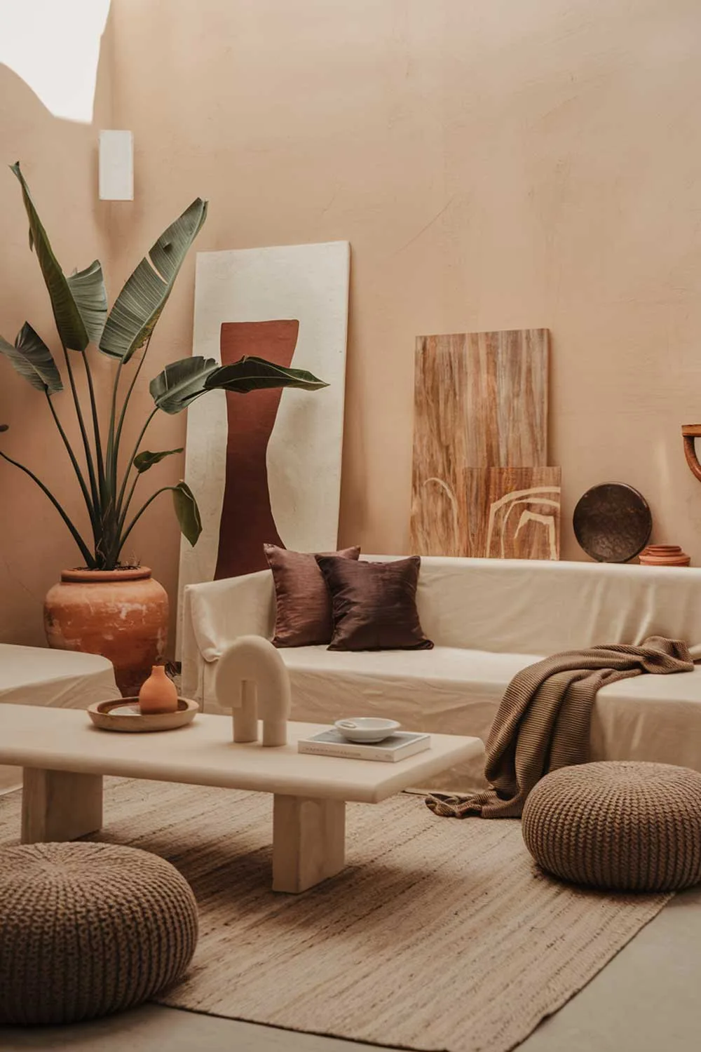 25 Inspiring Minimalist Living Room Ideas with Earth Tones 24 A cozy minimalist living room with earth tones. The room has a beige sofa, a few cushions in darker tones, a white coffee table, and a few decorative items. There's a large plant in a terracotta pot beside the sofa. The floor is covered with a beige rug. The walls have a few pieces of artwork. The lighting is soft and warm.