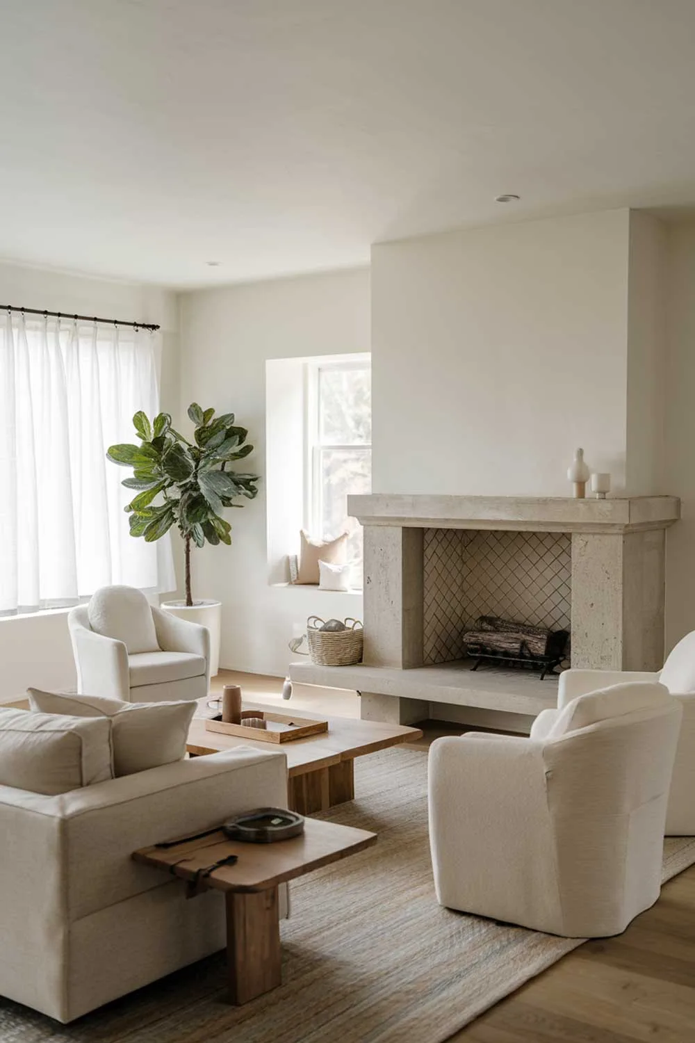 A photo of a cozy modern minimalist living room with a fireplace. The room has a beige sofa, a few white chairs, and a wooden coffee table. There's a potted plant near the window. The fireplace is made of stone and has a simple design. The walls and ceiling are painted white.