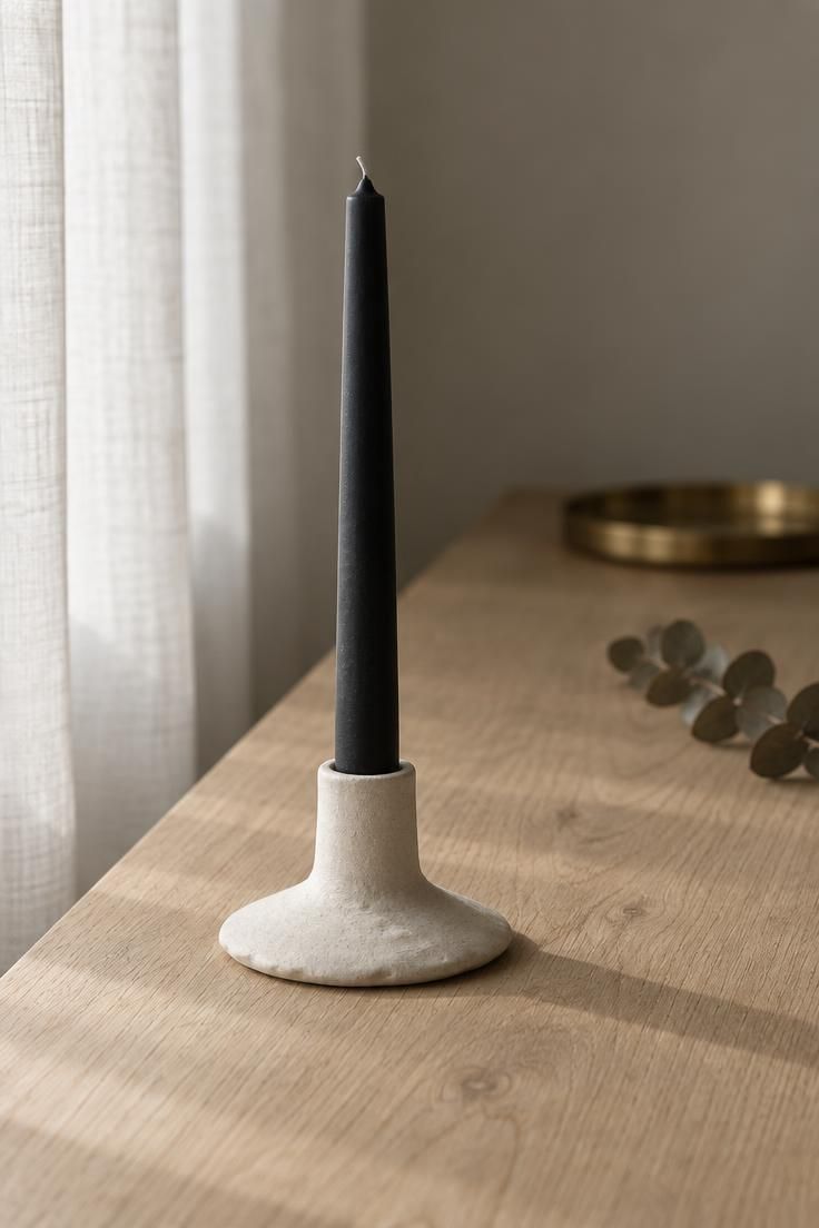 13 Warm Minimalist Halloween Ideas for a Calm Autumn Home 1 A slim matte black taper candle in a bone ceramic holder on a bare oak console with soft daylight from the left.