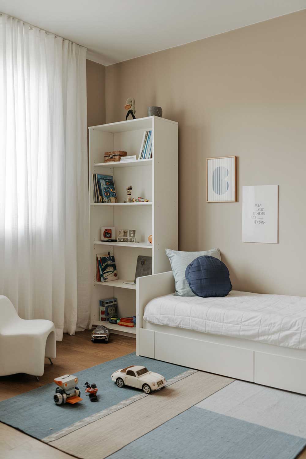 A minimalist boys bedroom with a white bed, a white bookshelf, and a blue rug. The bed has a blue pillow and a white pillow. There is a small white chair near the bed. The walls are painted a light beige color. The room has a few toys, including a car and a robot. There is a window with white curtains.