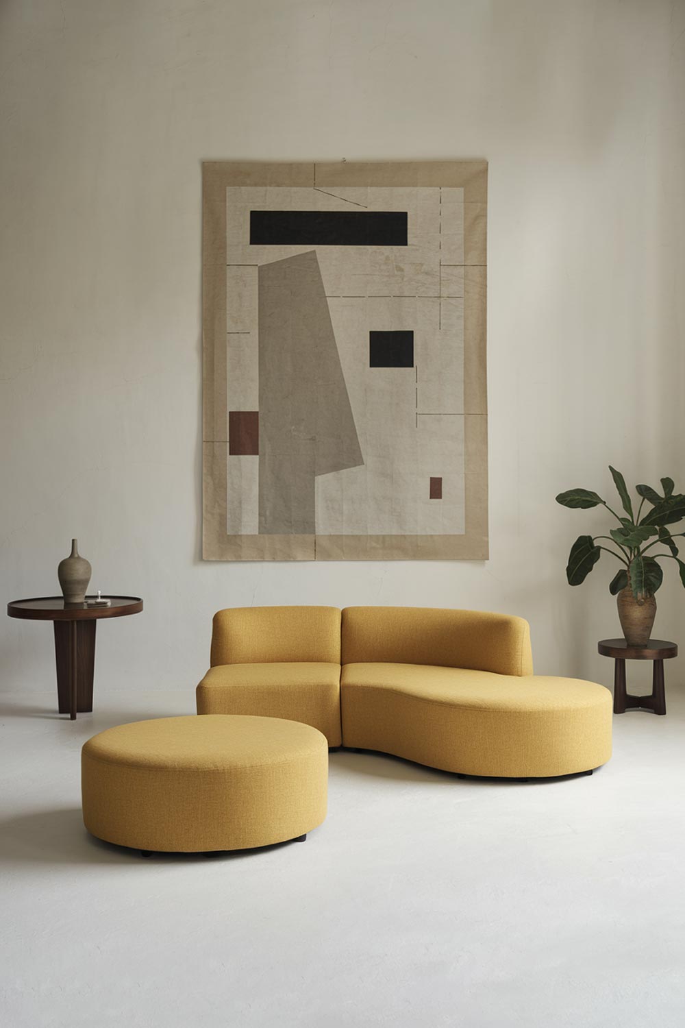 A minimalist living room with a yellow couch and an ottoman. The couch is placed at an angle, facing a wall with a large, abstract artwork. The room has a few other items, including a round table with a vase and a potted plant. The walls and floors are white.