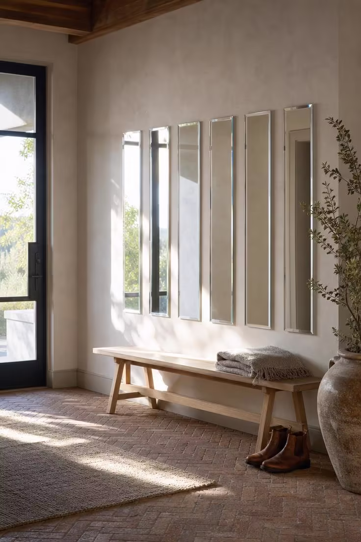 Six narrow beveled frameless mirror strips mounted vertically on a plaster entryway wall