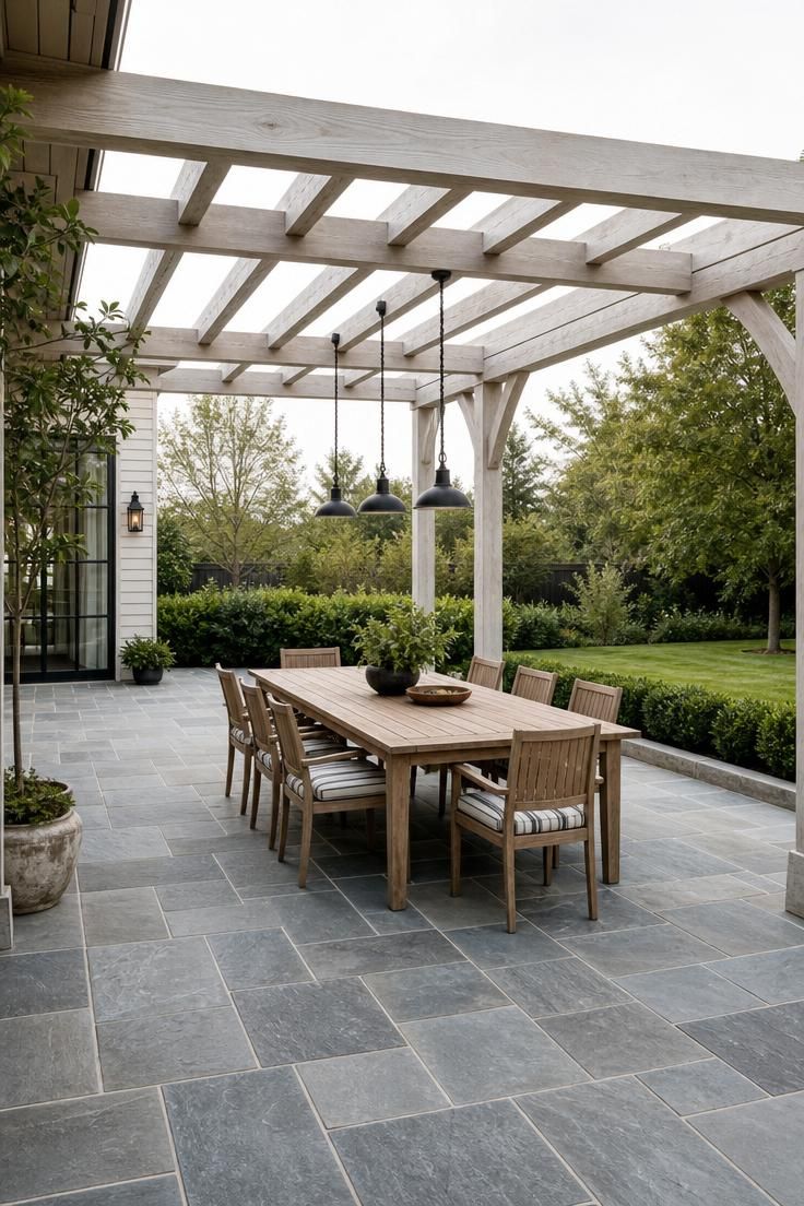 17 Sleek Modern Backyard Landscaping Plans Worth Copying 2 A bluestone slab dining terrace under a whitewashed beam pergola with pendant lights and a teak table set for eight on a soft afternoon.