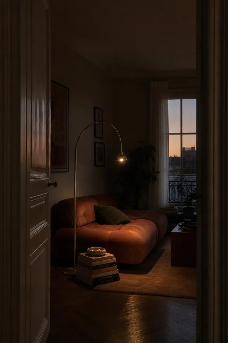 10 Modern Eclectic Apartment Ideas Full of Character 4 Brass arc floor lamp arching over a terracotta velvet sofa in a dim apartment living room.
