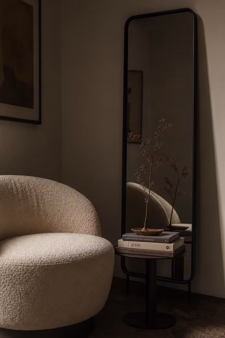 Boucle accent chair beside a matte black steel-framed mirror in moody, low-lit corner styling.