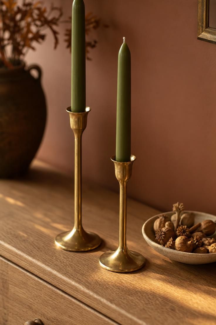 Pair of brass taper holders with olive dripless candles on a raw oak dresser in warm golden afternoon light