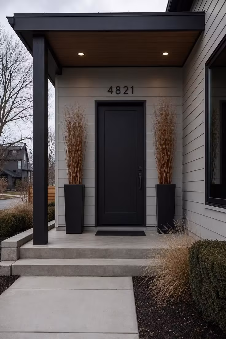 10 Modern Fall Porch Decor Ideas for a Cozy Welcome 6 Symmetrical black planters with curly willow flanking a modern matte black door with oversized house numbers.