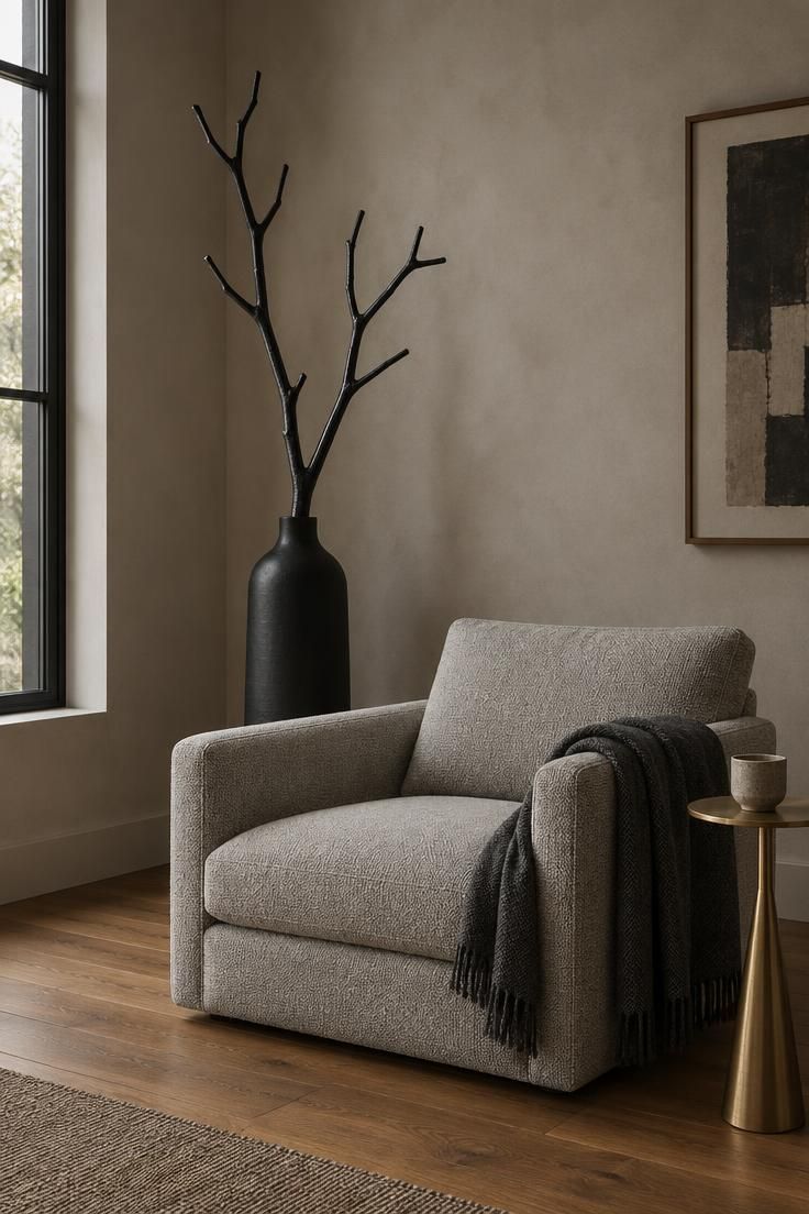 11 Moody Modern Halloween Decor Ideas for a Calm Home 7 Black-painted branches in a tall matte black floor vase behind a gray armchair in a dim corner.