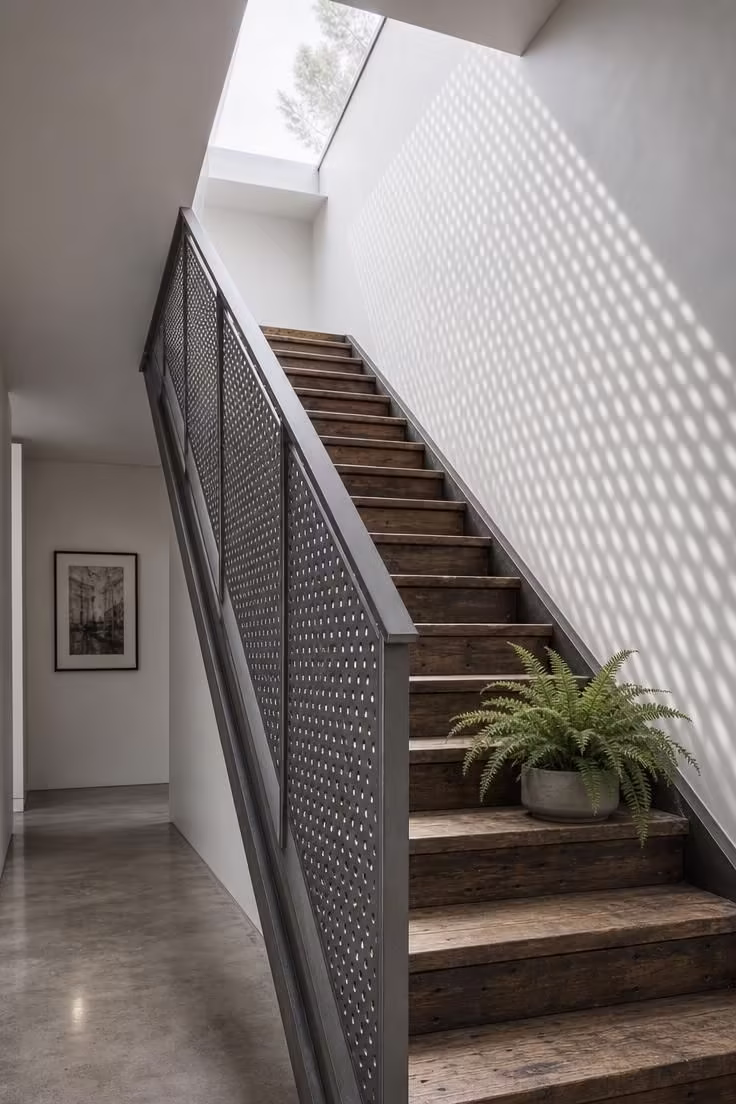 Perforated steel sheet stair railing with flat bar handrail and reclaimed wood treads under cool overcast skylight