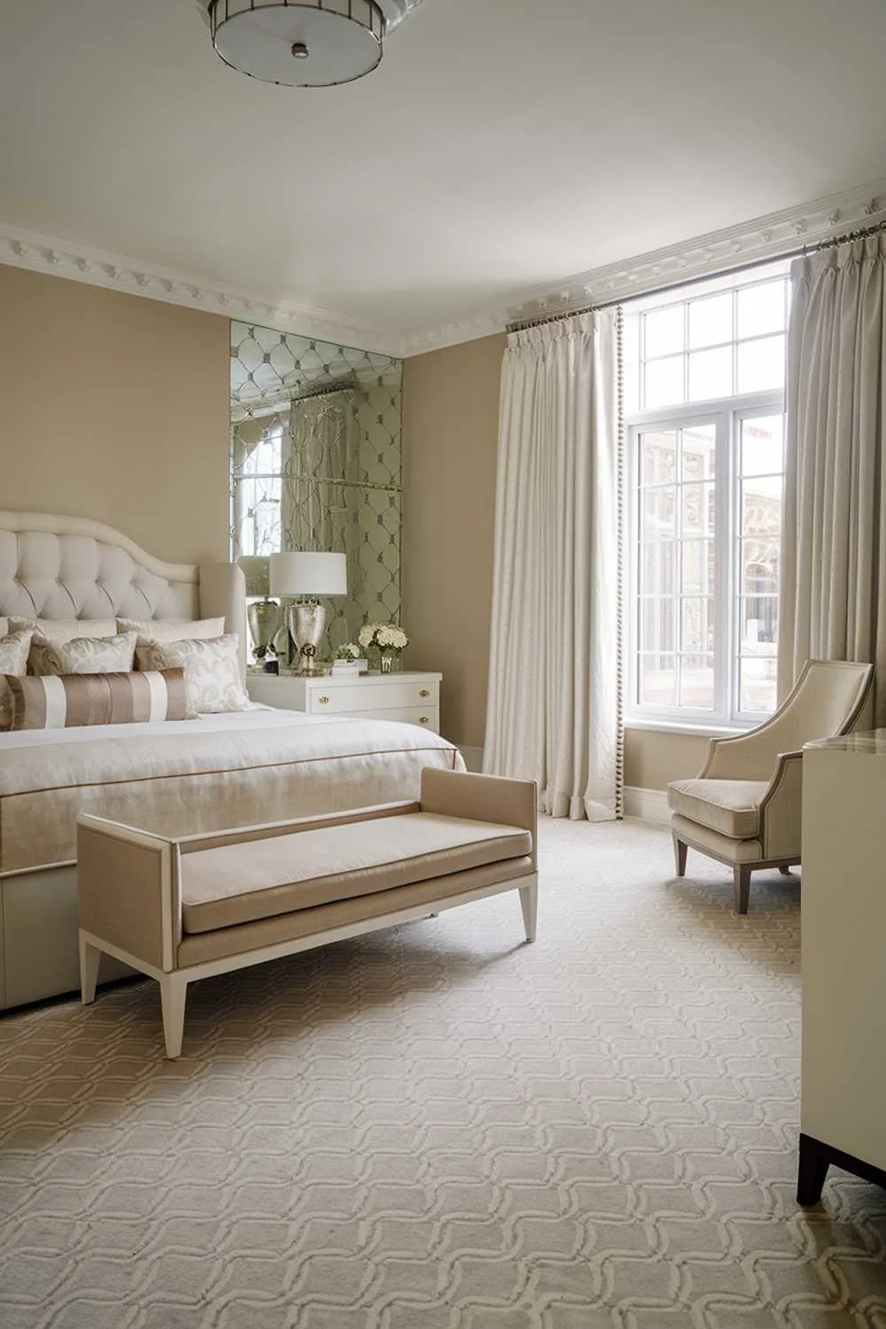 23 Modern Luxury Bedroom Design Ideas You'll Love 16 A classy modern luxury bedroom design. The room has a king-size bed with a beige headboard and a white bed frame. There's a beige chair near the bed. The room has a large window with white curtains. The floor is covered with beige and white patterned carpet. There is a white dresser with beige drawers near the bed. The walls are painted beige. The room has a white ceiling light fixture.