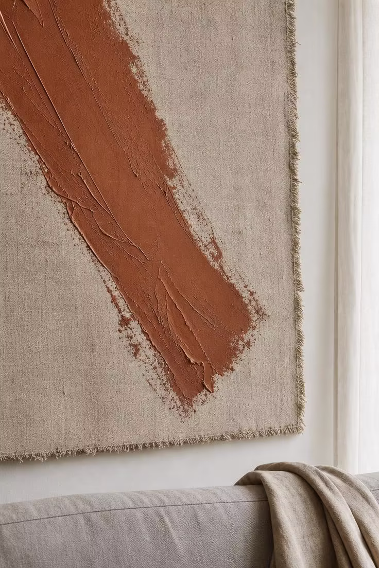 13 Bold Modern Wall Decor Ideas for a Polished Home 4 Close-up of an oversized raw linen canvas with a single bold burnt sienna brushstroke showing texture details in soft diffused light.