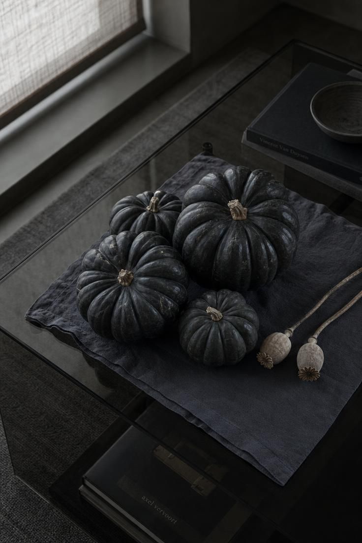 Near-black heirloom pumpkins grouped on a smoked-glass table in soft light.