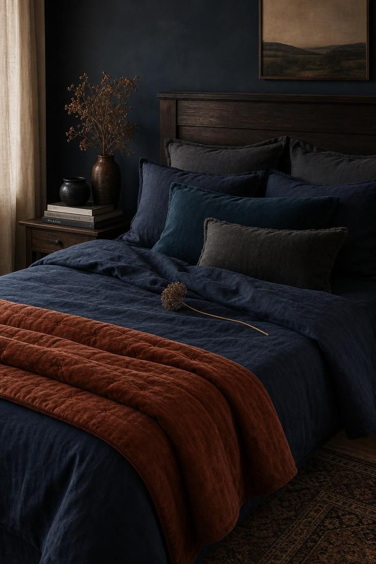 Bed layered in ink-blue linen and rust velvet under soft, diffused light.