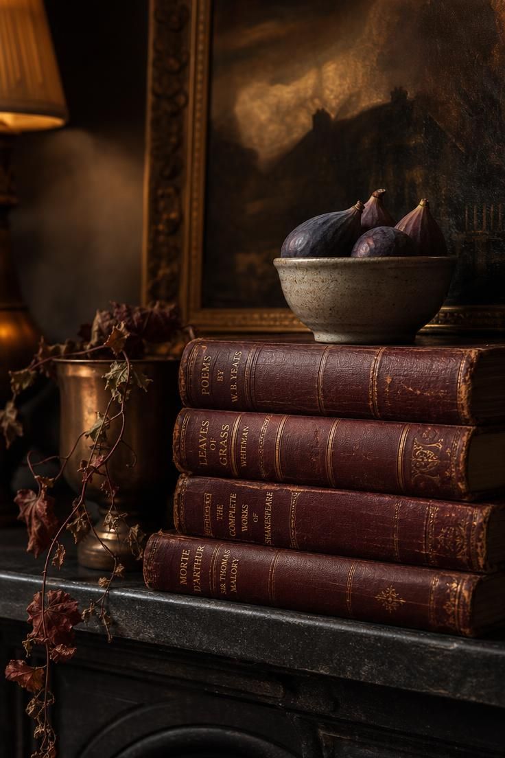 Leather-bound books topped with a dark fig bowl on a charcoal mantel in warm light.