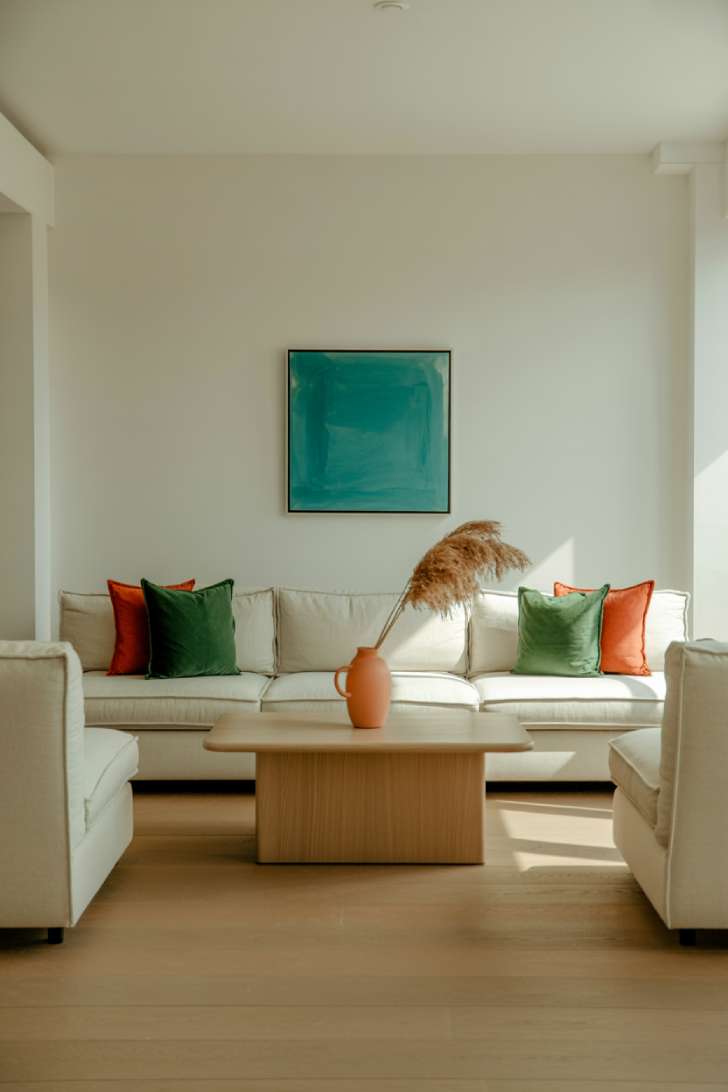 Cream sectional sofa with emerald green pillows, coral vase, and turquoise painting in a neutral living room