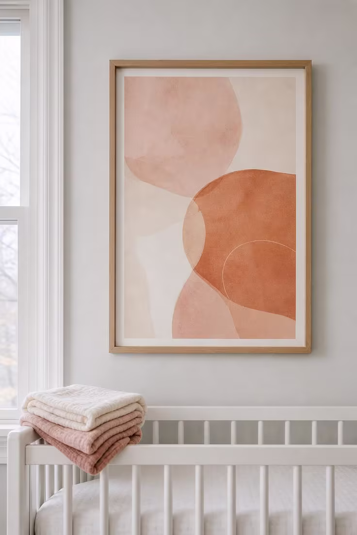 13 Stunning Nursery Wall Decor Ideas That Feel Timeless 6 Large abstract print in blush and terracotta inside a raw oak float frame above a white crib in cool morning light.