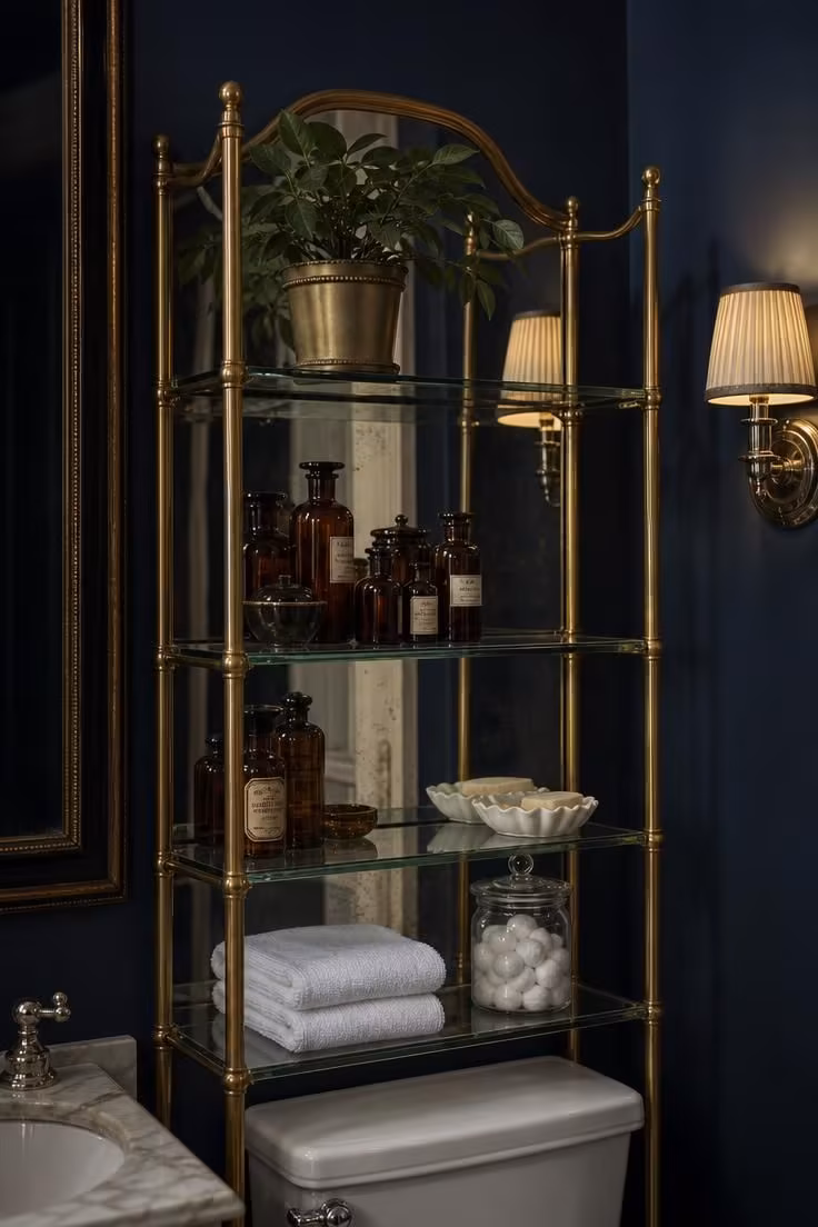 10 Over the Toilet Storage Ideas to End Clutter Now 9 Antique brass and glass etagere with a mirrored back panel over a toilet, holding towels and apothecary bottles.