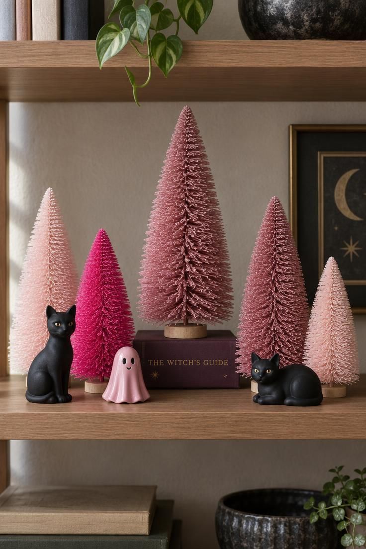 10 Dreamy Pink Halloween Decor Ideas for a Soft Spooky Look 7 Pink bottle-brush trees in blush, hot pink, and dusty rose with black cat figures and a pink ceramic ghost on an open shelf.