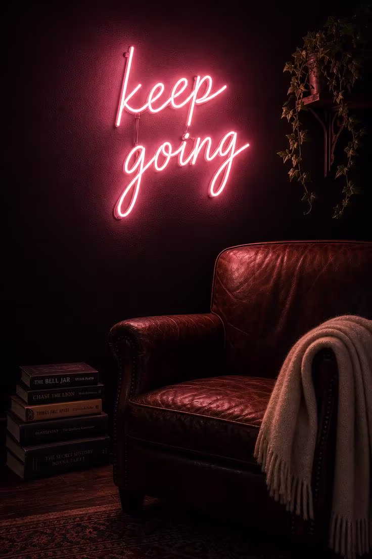 10 Charming Pink Wall Decor Ideas That Feel So Fresh 8 A pink neon sign reading keep going mounted on a dark charcoal wall above a leather armchair in a moody reading corner.