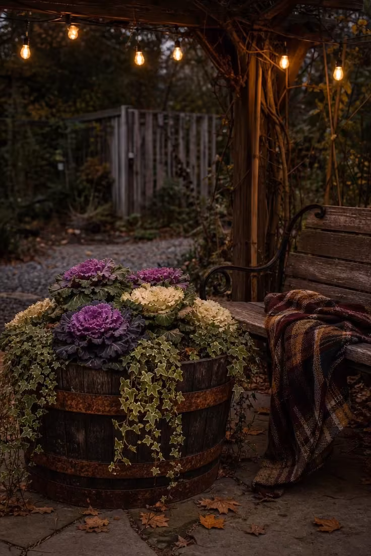 11 Warm Rustic Fall Decor Ideas for a Cozy Home Retreat 10 Whiskey barrel half-planter with ornamental kale and trailing ivy on a stone patio in moody low evening light with string lights above
