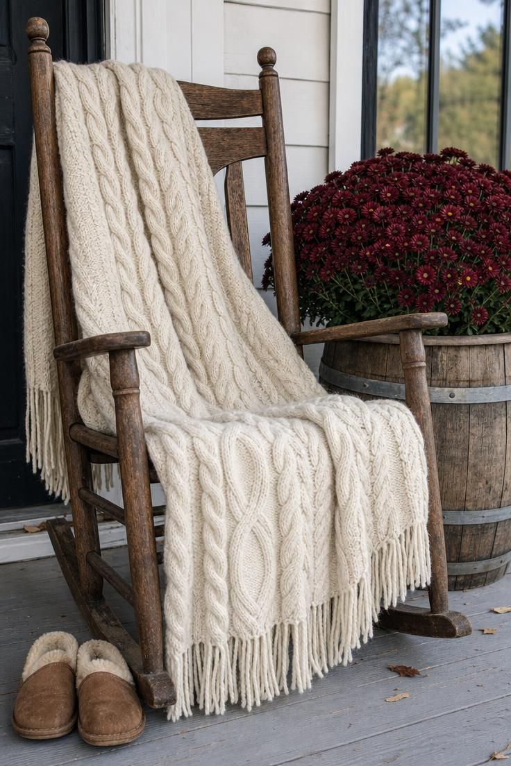11 Cozy Rustic Fall Porch Ideas for a Warm Welcome 8 A rocking chair with a cream cable-knit throw beside a barrel planter of burgundy mums in bright midday light.