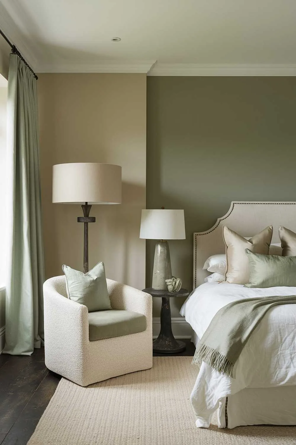 27 Must-See Sage Green Bedroom Ideas for Sweet Dreams 11 A bedroom with stylish decor. The room has a beige wall, a dark wooden floor, and a sage green accent wall. There's a white bed with beige pillows and a sage green throw blanket. There's a beige chair with a sage green cushion in the room. The room has a beige lampshade and a sage green lamp. The room has a beige rug.