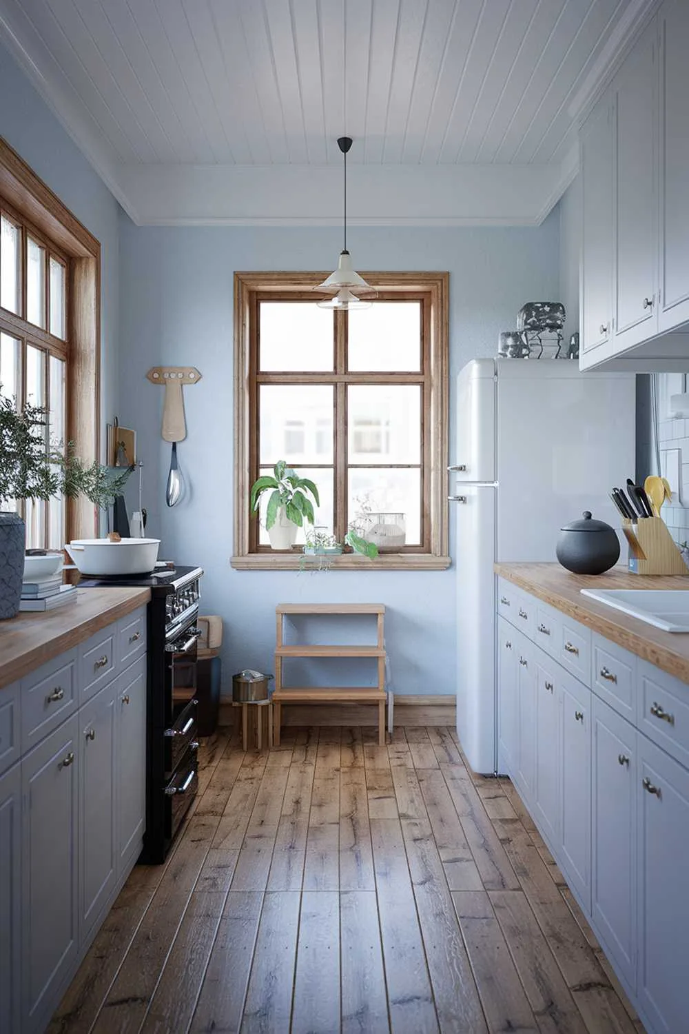 A cozy Scandinavian kitchen design with a wooden floor and light gray cabinets. There is a black stove, a white refrigerator, and a wooden countertop. A few items are placed on the countertop, including a white bowl, a dark gray pot, and a wooden utensil holder. The walls are painted in light blue. There's a wooden step stool near the refrigerator. The room has a window with wooden frames, and a potted plant is placed near the window. The space is illuminated by a pendant lamp above the sink.