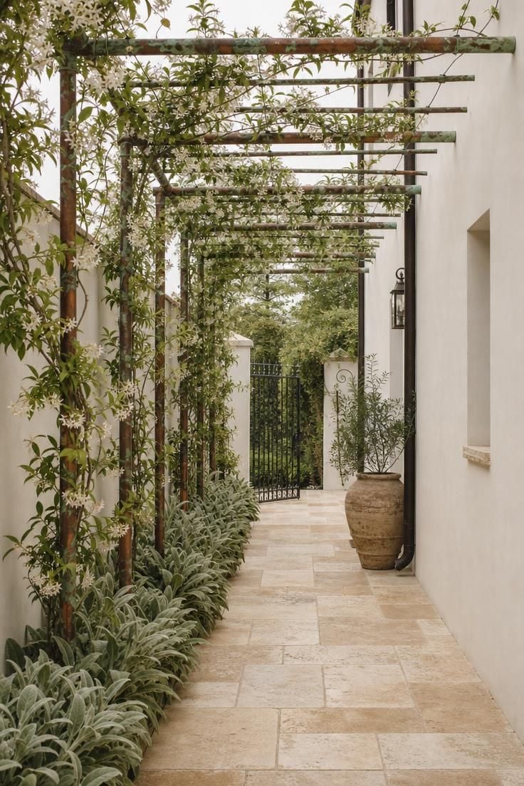 Tumbled travertine walkway beneath a copper pipe pergola with star jasmine in a narrow side yard