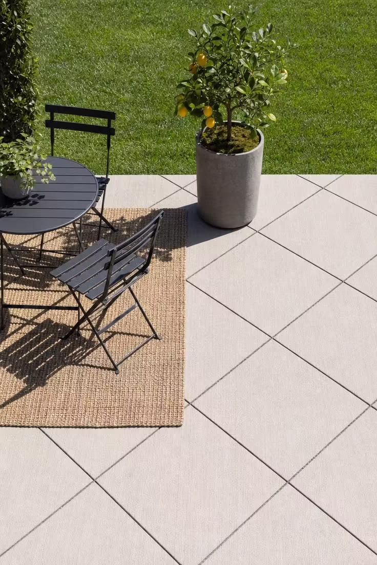 Broom-finish concrete patio with sawcut diamond grid pattern and black bistro set in bright midday light