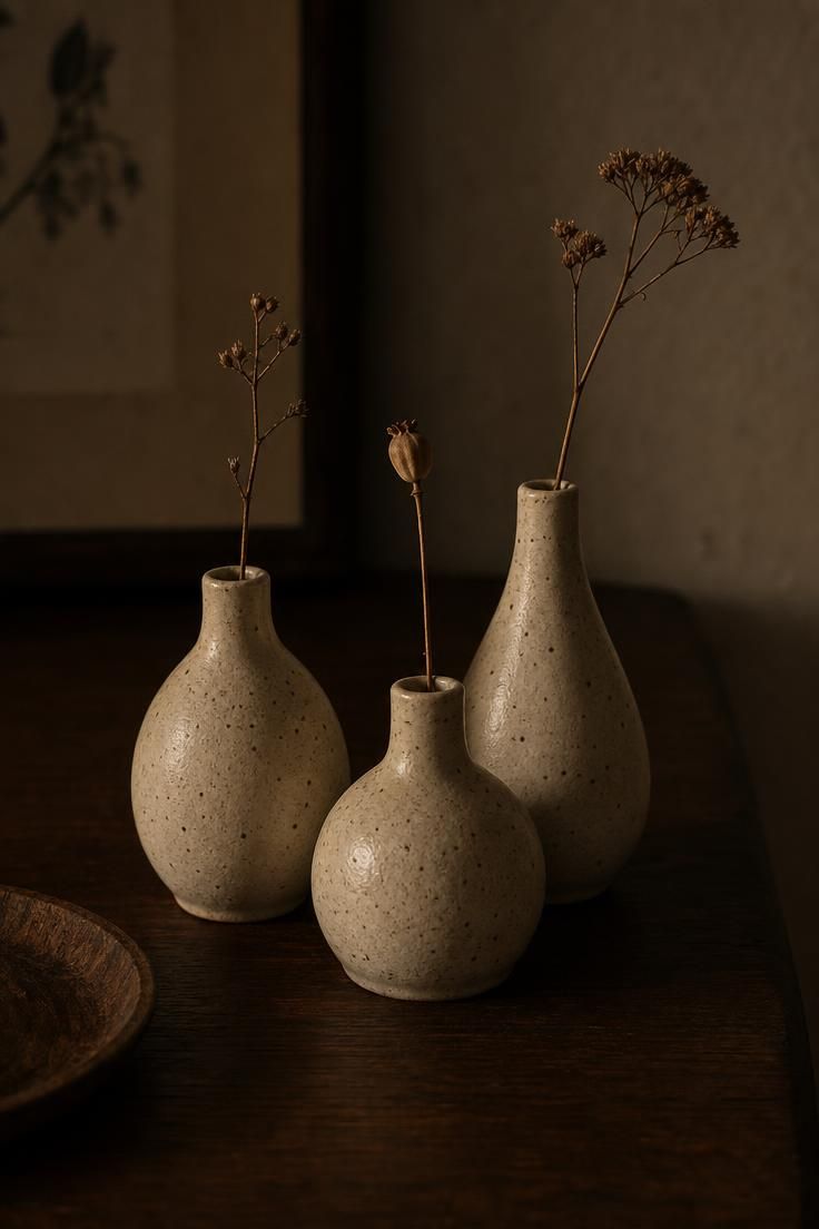 A trio of speckled ceramic bud vases with single dried stems, a bit of simple fall decor built from dried botanicals.