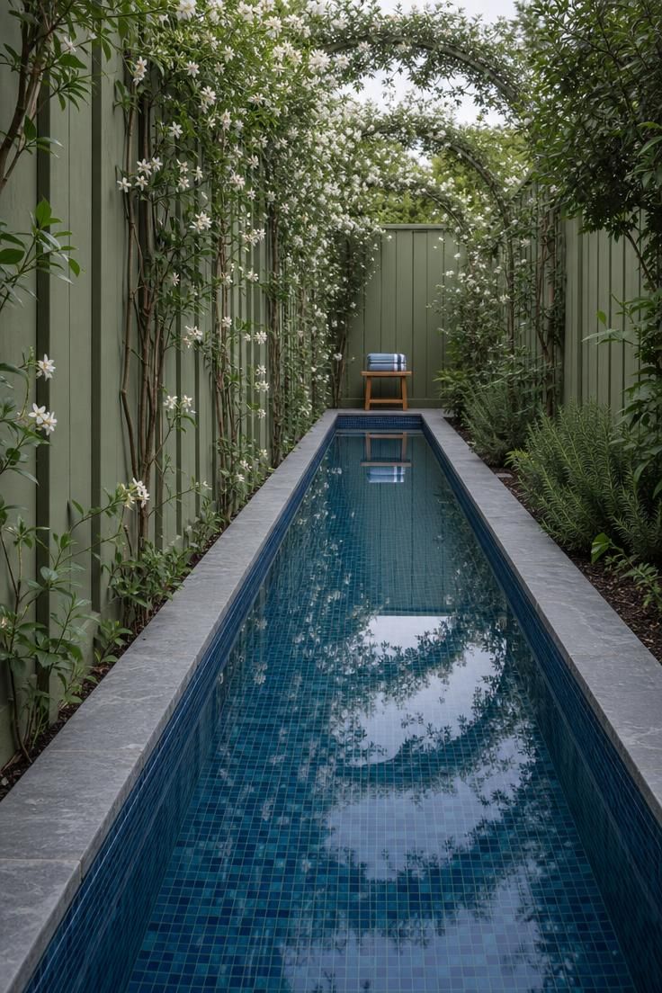 A narrow marine blue tile lap channel running along a sage green garden fence with climbing jasmine under cool overcast morning light.