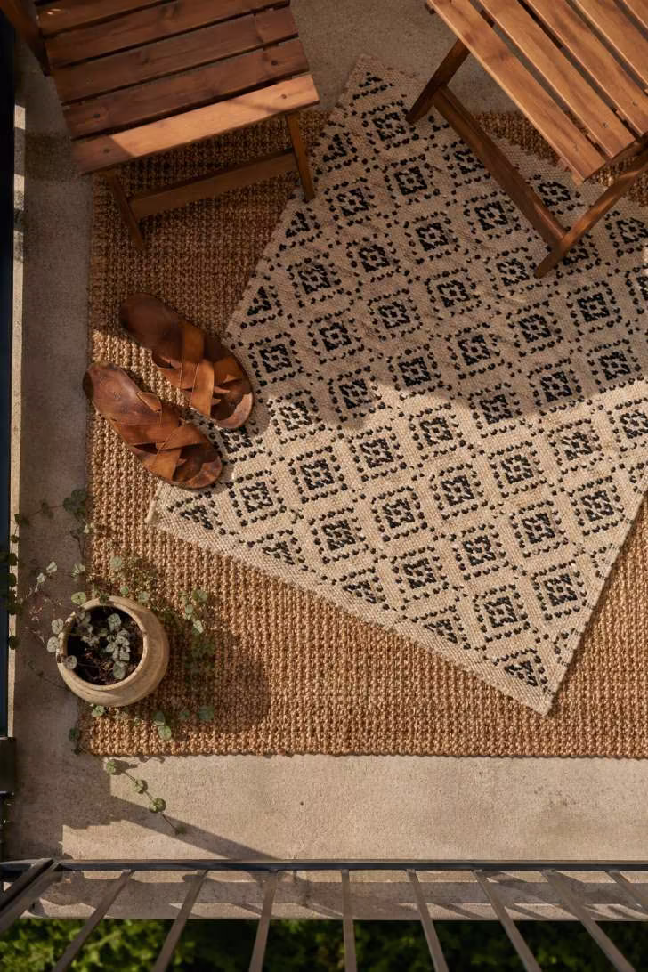 Overhead view of layered outdoor rugs on a small balcony with leather sandals and trailing plant