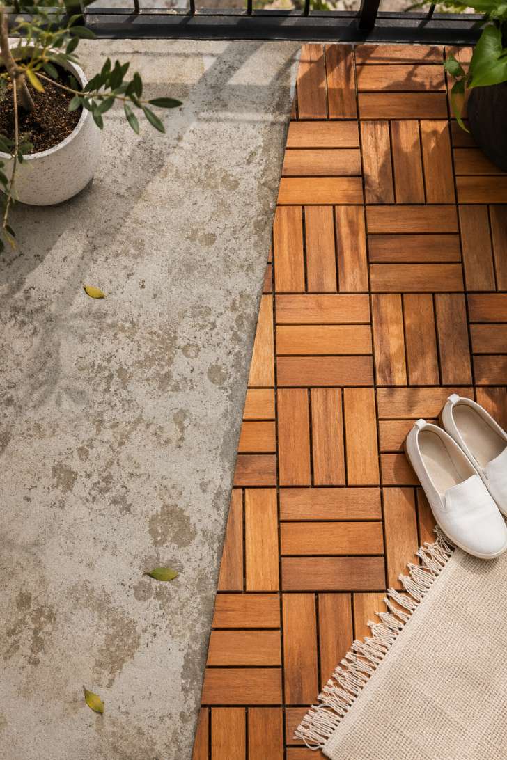 Overhead view of interlocking acacia wood deck tiles installed on a concrete balcony floor in herringbone pattern